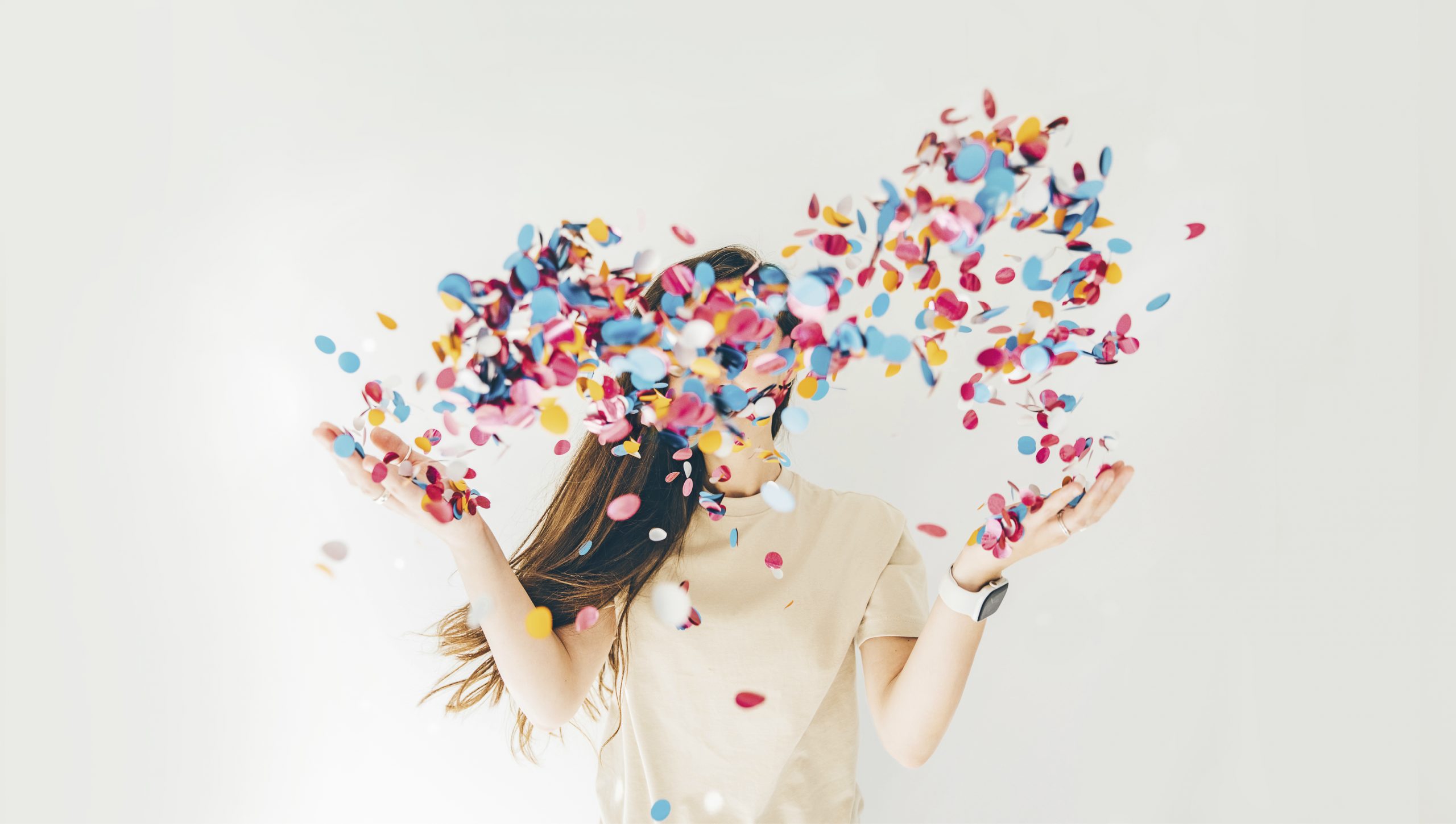 Eine Frau mit langen braunen Haaren wirf Konfetti in die Luft.