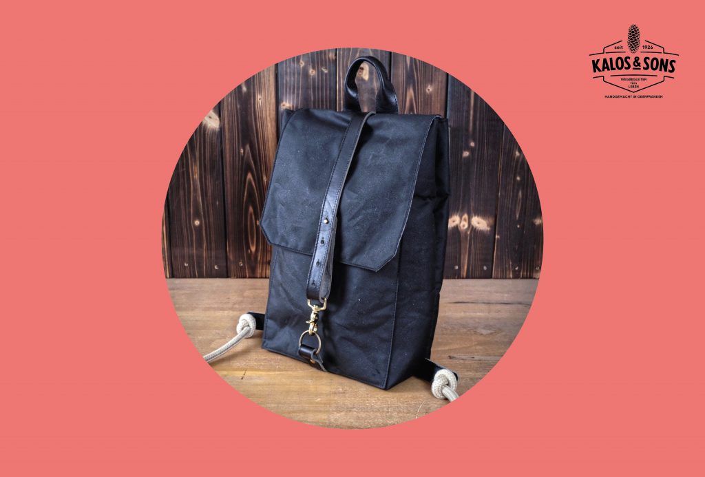 Schwarzer Rucksack auf Holztisch, eingefasst in rotem Rahmen mit Firmenlogo